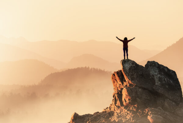 Adventurous Woman Hiking on the Rocky Coast with Mountains and Dramatic Sunset Sky.