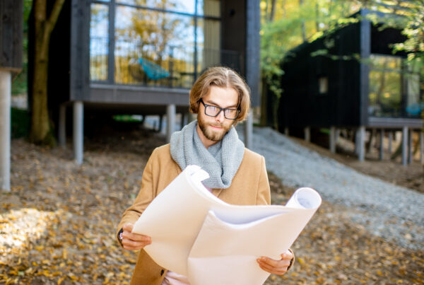 Portrait of a handsome man architect standing with drawings in front of the modern houses in the forest